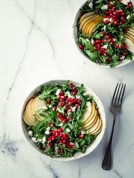 Vegan salad bowl with arugula, pear, pomegranate, coconut crumble or cottage cheese on marble tabletop. Vegan breakfast, vegetarian food, diet concept. Vertical. Top view or flat lay.