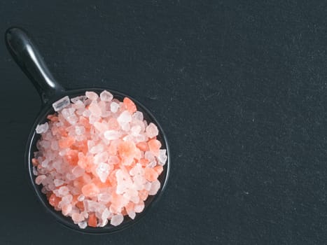 Himalayan pink salt in small black bowl on black stone background. Copy space