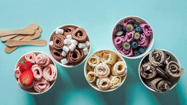 rolled ice creams in cone cups on blue background. Different iced rolls top view or flat lay. Thai style rolled ice cream