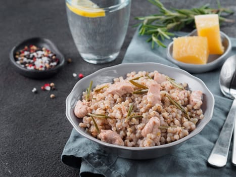 Raw buckwheat risotto with chicken meat and rosemary served parmesan cheese in gray plate on black cement background. Gluten-free and buckwheat recipe ideas. Copy space