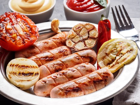 Chicken homemade sausages with sauces ketchup and mustard on black background. Grilled sausages and grilled vegetables in metal plate. Copy space.