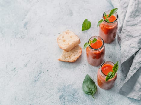 Delicious gaspacho soup in glass bottles. Traditional spanish cold soup puree gaspacho or gazpacho on gray cement background with copy space for text. View from above or top view or flat lay