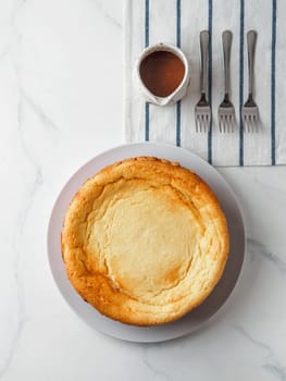 Plate with whole cheesecake pie on marble table. Classic cheesecake, caramel and dessert forks. Vertical. Top view or flat lay.