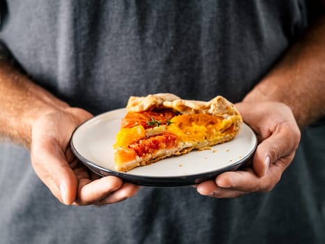 Hands takes plate with portion piece of pie. Savory fresh homemade tomato tart or galette. Healthy appetiezer - whole wheat or rye-wheat pie with tomatoes,cheese. Copy space for text