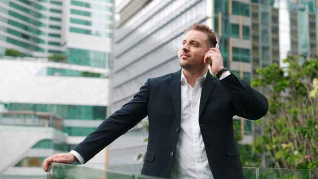 Close up of male leader listen headphone and dancing to relaxing music with cheerful and motivation. Skilled project manager enjoy to listen relaxed song while hold smart phone at urban city. Urbane.