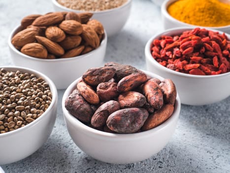 Raw cocoa bean in small white bowl and other superfoods on background. Selective focus. Different superfoods ingredients. Concept and illustration for superfood and detox food
