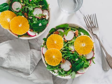 Vegan salad bowl with oranges, spinach, arugula, radish, nut. Top view. Vegan breakfast, vegetarian food, diet concept. Two bowls with salad on white marble tabletop