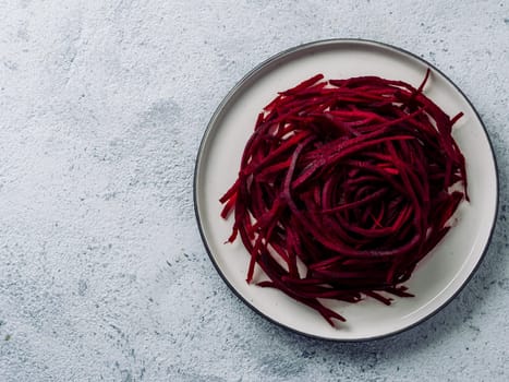 Raw beetroot noodles top view. Vegetable noodles - beet spaghetti on plate over gray cement background. Copy space for text. Clean eating, raw vegetarian food concept.