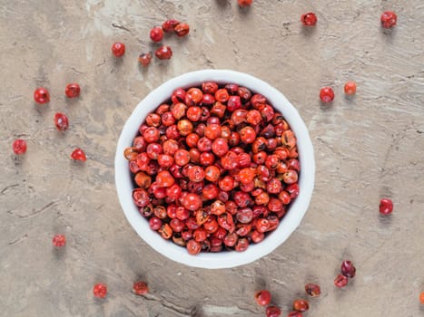 Pile with dried pink pepper berries on brown concrete background. Close up view of pink peppercorn. Top view or flat-lay.