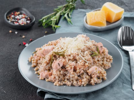 Raw buckwheat risotto with chicken meat and rosemary served parmesan cheese in gray plate on black cement background. Gluten-free and buckwheat recipe ideas. Copy space