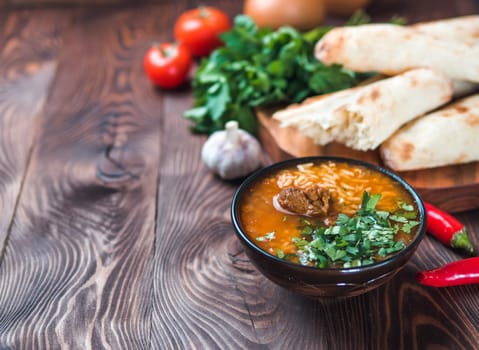 Traditional Georgian kitchen-soup Kharcho with meat, rice and fresh cilantro. Spicy soup Kharcho on wooden table with traditional bread Shotis Puri and vegetables. Selective focus. Copy space for text