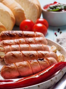 Close up view of chicken homemade sausages with buns bread. Grilled sausages and grilled vegetables in craft trendy plate. Home hotdogs. Vertical.