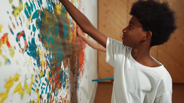 Back view of happy african boy painted the stained wall with colorful hand while wearing casual white shirt in art lesson.Smart student use hand print to make creative artwork. Education. Edification.