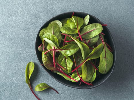 Fresh salad of green chard leaves or mangold on gray stone background. Flat lay or top view fresh baby beet leaves in craft ceramic bowl.