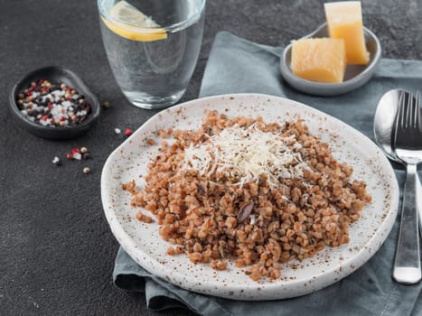 Buckwheat risotto with dried mushrooms in craft plate on black cement background. Gluten-free and vegetarian buckwheat recipe ideas. Copy space