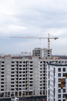 A crane and a building under construction against a blue sky background. Builders work on large construction sites, Building a house is not necessary for new high-rise buildings