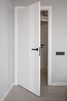 An open white door with a manual one in a renovated apartment. Moving to a new apartment. Doorknob on an open door with a ladder in the room during renovation and painting work.