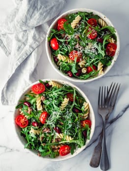 Warm salad with tuna, arugula, tomatoes ,red bean, pasta.Idea and recipe for healthy lunch or dinner.Two bowls with warm salads on marble table. Ideas and recipes for healthy dinner or lunch. Vertical