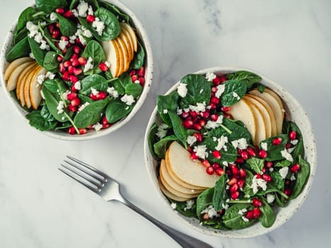 Fresh salad with baby spinach, pear, pomegranate and cottage cheese. Two bowls with delicious summer fruit salad on marble table. Copy space for text. Ideas and recipes for healthy breakfast or lunch