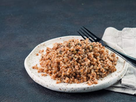 Buckwheat risotto with dried mushrooms in craft plate on black cement background. Gluten-free and vegetarian buckwheat recipe ideas. Copy space