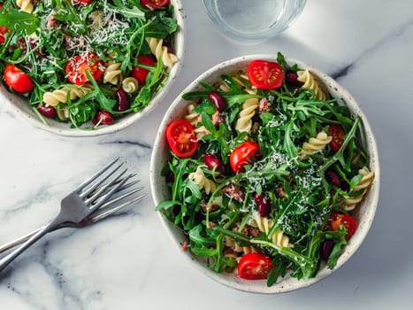 Warm salad with tuna, arugula, tomatoes, red bean, pasta. Idea and recipe for healthy lunch or dinner. Two bowls with warm salads on marble tabletop. Idea healthy dinner. Top view Copy space for text.