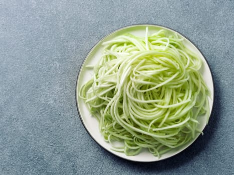 Zucchini noodles on plate.Vegetable noodles -green zoodles or courgette spaghetti on plate over gray stone background.Clean eating, raw vegetarian food concept.Copy space for text.Top view or flat lay