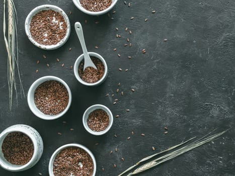 flax seeds and dry rye ear on dark background. Set of small bowls with organic flax seed or linen seed. Flax seeds is rich in omega-3 fatty acid. Copy space. Top view or flat-lay.