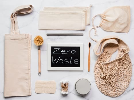 Zero waste concept. Textile eco bags, metal straws, eco-friendly kitchen tools, bamboo toothbrush and cotton buds, reusable cotton pads on white marble background. Top view or flat lay
