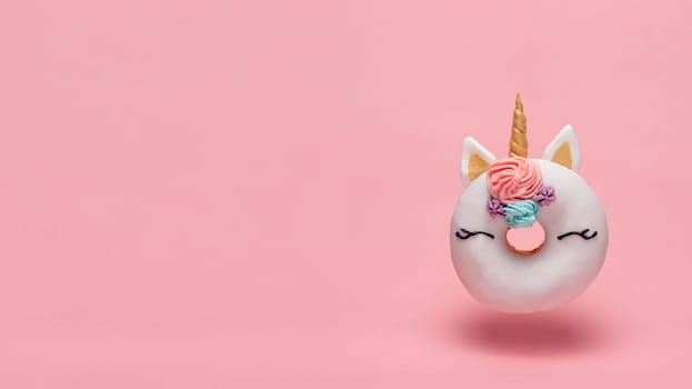 Unicorn donut hovers in air over pink background. Trendy donut unicorn with white glaze flying. Copy space for text.
