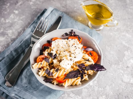 Tasty italian fusilli pasta with cherry, mozarella or buratta cheese and fresh basil. Dish with pasta on gray concrete background. Copy space. Healthy food concept and recipe idea.