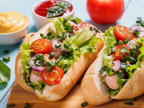 Close up view of homemade hotdogs with chicken, sausages, fresh vegetables, ketchup and mustard sauce on blue wooden background. Hot-dogs with tomatoes, onion, basil, letucce and spices.