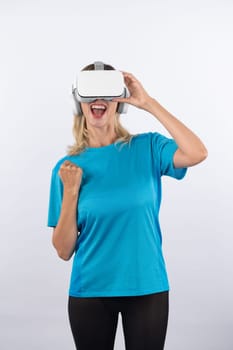 Caucasian happy girl holding VR glasses and making winner gesture. Skilled woman celebrate while winning game by using VR headsets and standing at pink background. Technology innovation. Contraption.