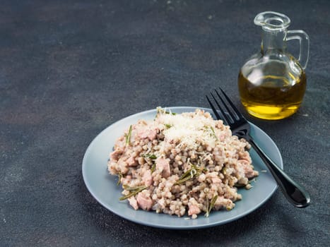 Raw buckwheat risotto with chicken meat and rosemary served parmesan cheese in gray plate on black cement background. Gluten-free and buckwheat recipe ideas. Copy space