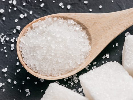 Granulated sugar in wooden spoon extreme close up. Background of sugar cubes and sugar in spoon. White sugar on black background.