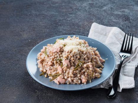 Raw buckwheat risotto with chicken meat and rosemary served parmesan cheese in gray plate on black cement background. Gluten-free and buckwheat recipe ideas. Copy space