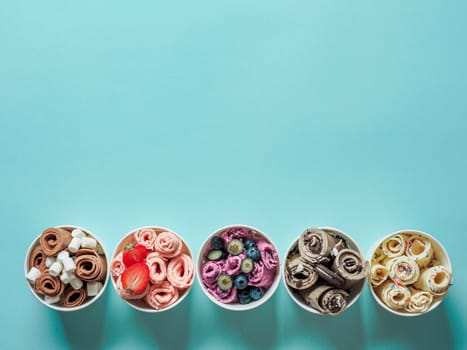 rolled ice creams in cone cups on blue background. Different iced rolls top view or flat lay. Thai style rolled ice cream with copy space for text or design