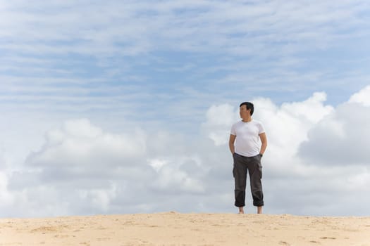 A man stands on a beach looking out at the ocean. The sky is cloudy, but the sun is still shining through the clouds. The man is lost in thought