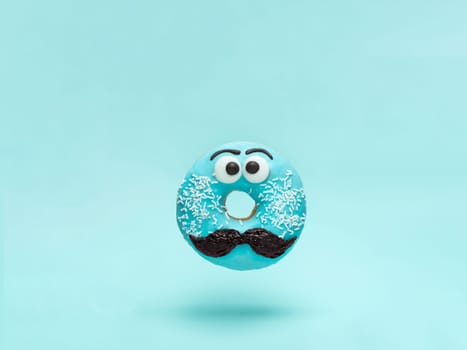 Blue glazed donut with mustache. Flying blue doughnut with funny face with mustache over blue background. Copy space for text. Masculinity or father day concept.