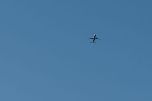 A commercial airplane soaring high above the clouds with blue sky in the background.