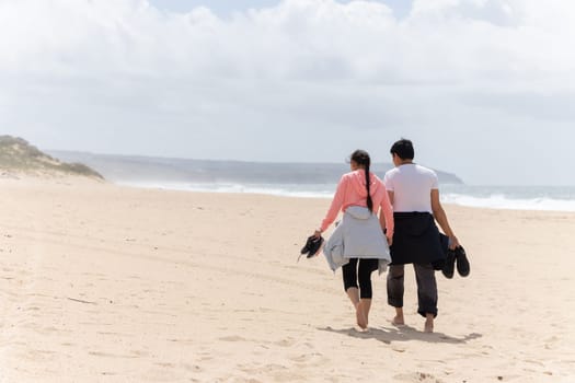 A couple walking on a beach with a man carrying a camera. The woman is wearing a pink shirt