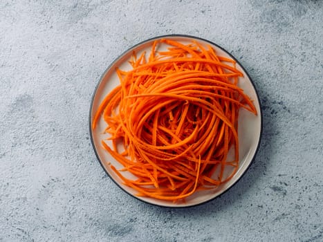 Carrot noodles on plate overhead. Vegetable noodles - orange sweet carrot spaghetti on plate over graybackground. Clean eating, raw vegetarian food concept. Flat lay or top view. Copy space for text