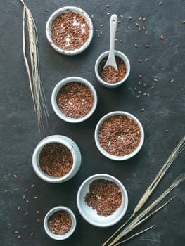 flax seeds and dry rye ear on dark background. Set of small bowls with organic flax seed or linen seed. Flax seeds is rich in omega-3 fatty acid. Vertical. Copy space. Top view or flat-lay.