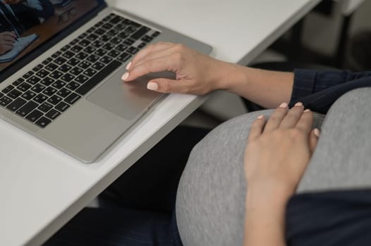 A pregnant woman works on a laptop in the office. Close-up of the tummy