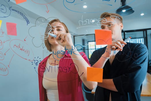 Couple of young creative start up business people brainstorming idea and solving problems by using sticky note and mind map at glass board, meeting room. discussing, working together. Immaculate.