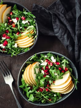 Vegan salad bowl with arugula, pear, pomegranate, coconut crumble or cottage cheese on black background.Vegan breakfast,vegetarian food,diet concept.Vertical.Top view or flat lay.Copy space for text
