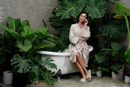 Tropical and exotic spa garden with bathtub in modern hotel or resort with young woman in bathrobe enjoying leisure and wellness lifestyle surrounded by lush greenery foliage background. Blithe