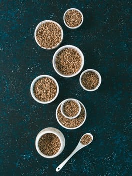 Hemp seeds in small white bowls and spoon on dark blue tabletop. Set of small bowls with raw organic unrefined hemp seed. Superfood and vegan concept. Top view or flat lay.Copy space for text.Vertical