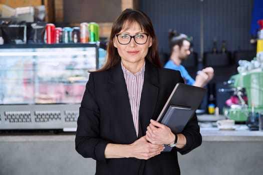 Portrait of confident business woman accountant financier lawyer small business owner. Successful middle-aged female with laptop in hands looking at camera, background coffee shop cafeteria restaurant
