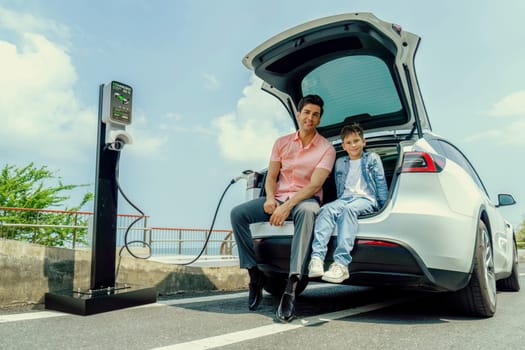 Family road trip vacation traveling by the sea with electric car, father and son recharge EV car with green and clean energy. Natural travel and eco-friendly car for sustainable environment. Perpetual