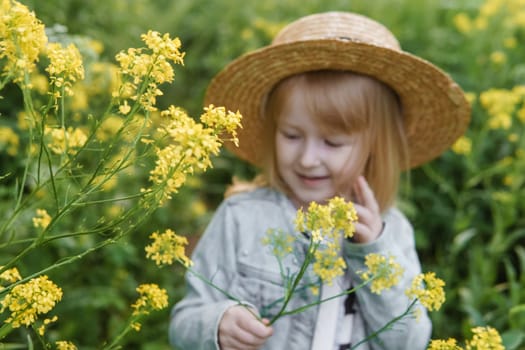 Blonde girl in a field with yellow flowers. A girl in a straw hat is picking flowers in a field. A field with rapeseed